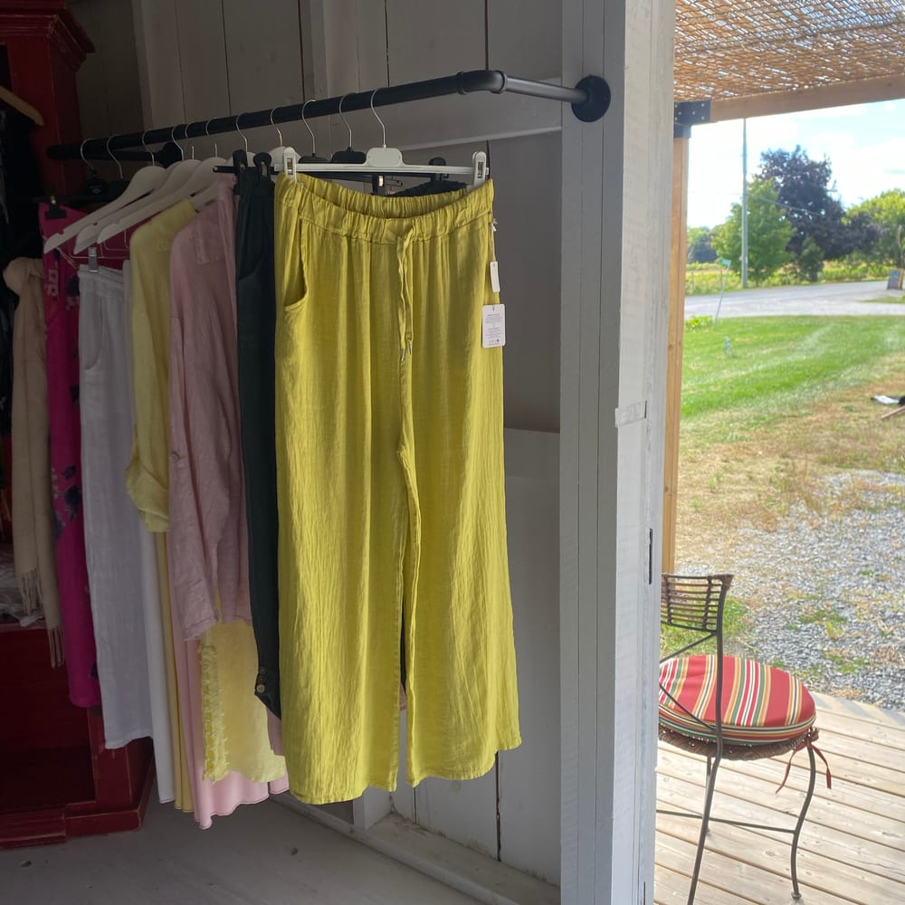 Inside the shed: a rail of linen in pink, white and chartreuse against white plank walls, with the door standing open onto the deck